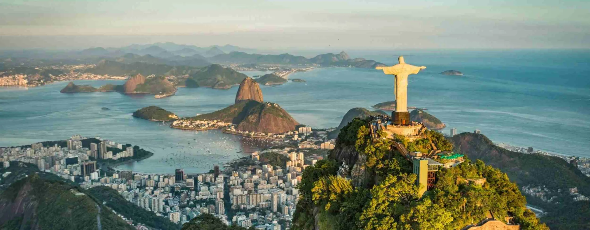 Cristo Redentor sobre o Rio de Janeiro no fim de tarde, com o Pão de Açúcar, a enseada de Botafogo e a cidade lá embaixo